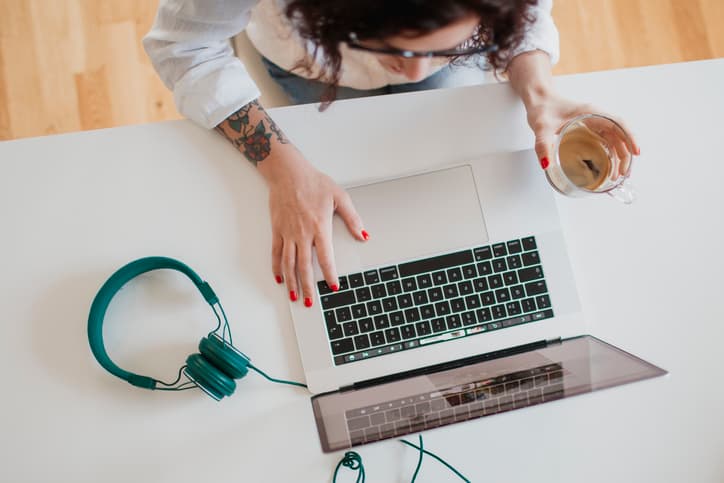 A top down view of a woman on her laptop with headphones sitting next to it.