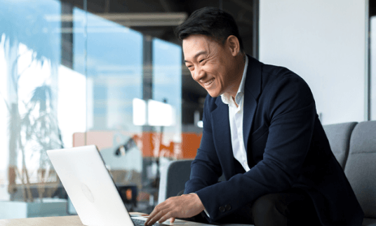 Man smiling gleefully at his laptop screen in the office.