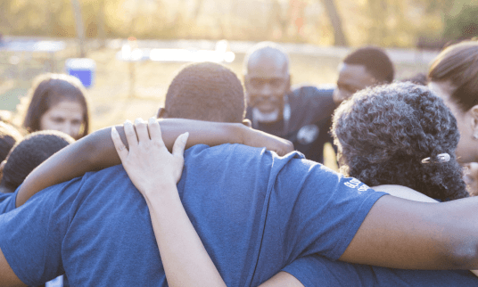 A group of social workers shares a group hug before an outdoor community event.